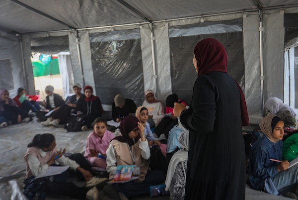 طلاب يتلقون دروسهم جلوسًا على الأرض داخل خيام تفتقر إلى المقاعد والتجهيزات المدرسية في مركز سرايا التعليمي بقطاع غزة، 11 أكتوبر/تشرين الأول 2026. (تصوير: محمد صالحة)