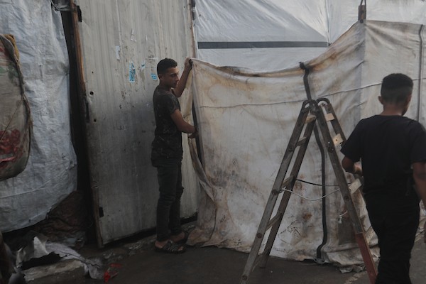 تحت أمطار غزة، يسير فلسطينيون نازحون وسط ظروف معيشية قاسية، فيما يحاول آخرون تغطية خيامهم لمنع تسرب مياه الأمطار إليها، في 18 أكتوبر/تشرين الأول 2026.تصوير: محمد صالحة