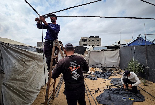 فلسطينيون يستخدمون قضبانًا معدنية انتشلوها من أنقاض منازل مدمرة لإقامة خيام تؤوي عائلات نازحة في منطقة المواصي بخان يونس، في 12 أكتوبر/تشرين الأول 2026، استعدادًا لفصل الشتاء.(تصوير: طارق محمد)