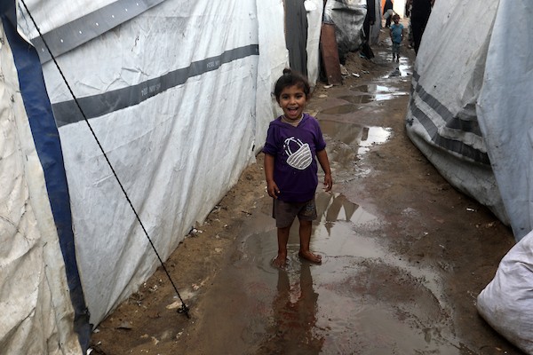 تحت أمطار غزة، يسير فلسطينيون نازحون وسط ظروف معيشية قاسية، فيما يحاول آخرون تغطية خيامهم لمنع تسرب مياه الأمطار إليها، في 18 أكتوبر/تشرين الأول 2026.تصوير: محمد صالحة