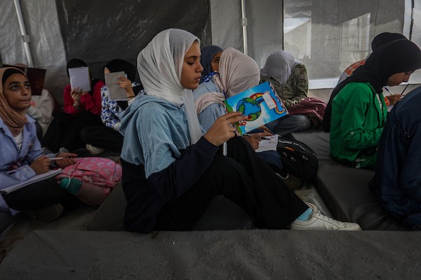 طلاب يتلقون دروسهم جلوسًا على الأرض داخل خيام تفتقر إلى المقاعد والتجهيزات المدرسية في مركز سرايا التعليمي بقطاع غزة، 11 أكتوبر/تشرين الأول 2026. (تصوير: محمد صالحة)