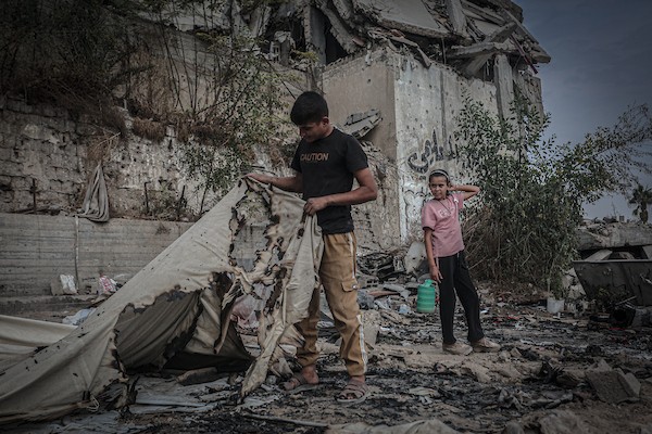 نازحون فلسطينيون يتفقدون بقايا خيامهم وممتلكاتهم التي أتت عليها النيران إثر غارة إسرائيلية قرب مفترق الشجاعية شرقي مدينة غزة، 26 أكتوبر 2026. (تصوير: بلال أسامة)