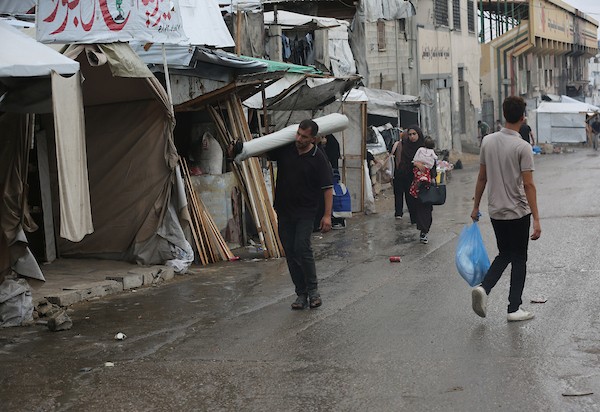 تحت أمطار غزة، يسير فلسطينيون نازحون وسط ظروف معيشية قاسية، فيما يحاول آخرون تغطية خيامهم لمنع تسرب مياه الأمطار إليها، في 18 أكتوبر/تشرين الأول 2026.تصوير: محمد صالحة