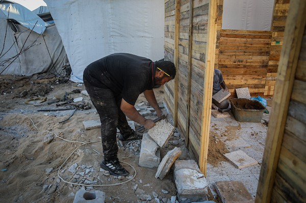 الفلسطيني هشام حميد يبني مأوى لعائلته من أخشاب المساعدات والطين قرب أنقاض منزله غرب مدينة غزة، استعدادًا لبرد الشتاء، 28 أكتوبر/تشرين الأول 2026. (تصوير: محمد صالحة)