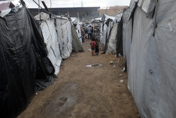 تحت أمطار غزة، يسير فلسطينيون نازحون وسط ظروف معيشية قاسية، فيما يحاول آخرون تغطية خيامهم لمنع تسرب مياه الأمطار إليها، في 18 أكتوبر/تشرين الأول 2026.تصوير: محمد صالحة