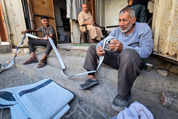 الخياط الفلسطيني شعبان الطباش يصلح أغطية بلاستيكية وقماشًا مشمعًا لتقوية خيام النازحين وحمايتها من برد الشتاء وأمطاره، في خان يونس جنوب قطاع غزة، 4 أكتوبر/تشرين الأول 2026. (تصوير: طارق محمد)