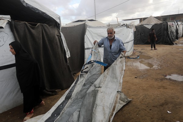 تحت أمطار غزة، يسير فلسطينيون نازحون وسط ظروف معيشية قاسية، فيما يحاول آخرون تغطية خيامهم لمنع تسرب مياه الأمطار إليها، في 18 أكتوبر/تشرين الأول 2026.تصوير: محمد صالحة